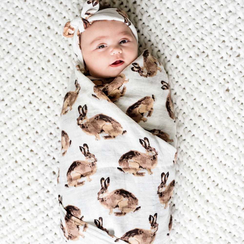 Milkbarn bamboo muslin swaddle wrapped around a newborn with a bunny print and white bow headband