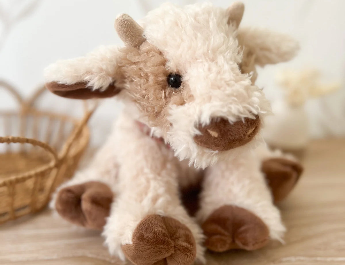 Mon Ami Caden Cow Plush sitting on a wood floor beside a wicker basket