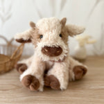 Mon Ami Caden Cow Plush, close-up of the fluffy cream cow with brown hooves on a wood floor