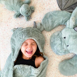Laughing child in the Mon Ami Dax Dragon Plush Blanket hood lying among dragon plush toys