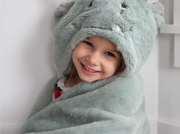 Smiling child wrapped in the Mon Ami Dax Dragon Plush Blanket with the dragon hood up