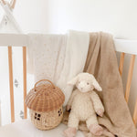 Mon Ami Lafayette the Lamb plush sitting in a crib with a rattan basket and blankets