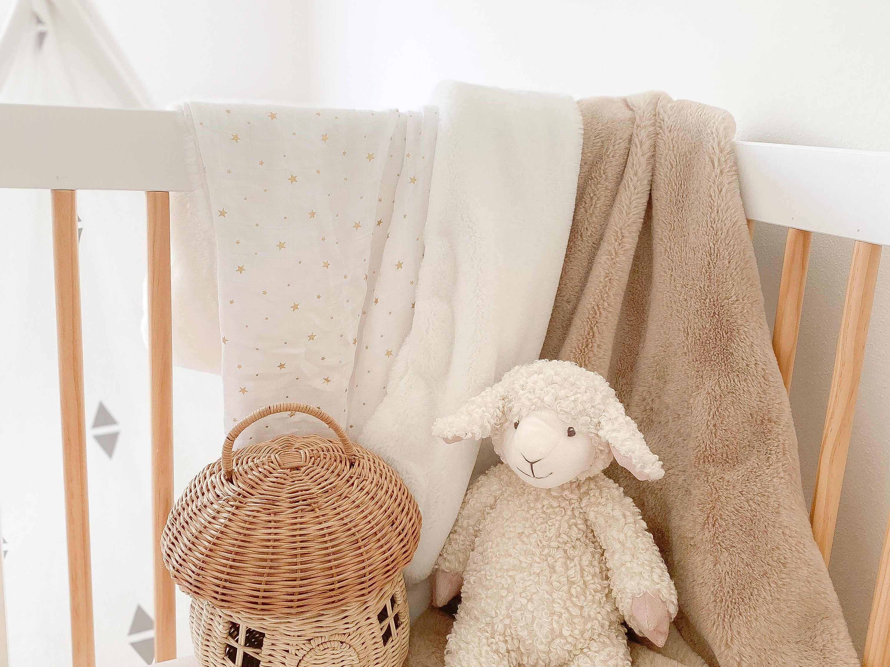 Mon Ami Lafayette the Lamb plush sitting in a crib with a rattan basket and blankets