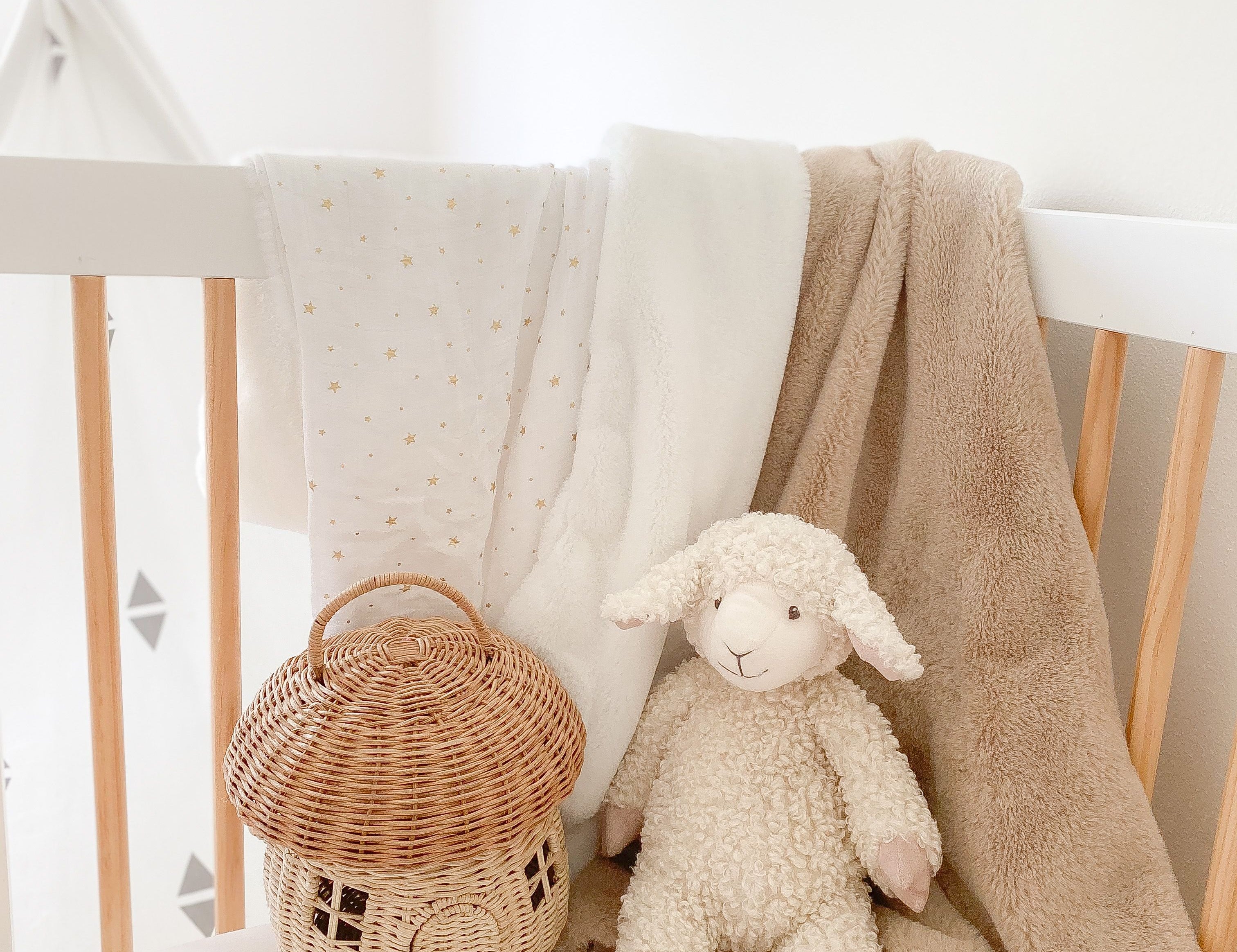 Mon Ami Lafayette the Lamb plush sitting in a crib with a rattan basket and blankets