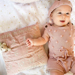 Baby in a pink outfit lying beside the Mon Ami My First Year Advent Pillow in Princess