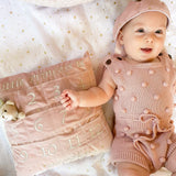 Baby in a pink outfit lying beside the Mon Ami My First Year Advent Pillow in Princess