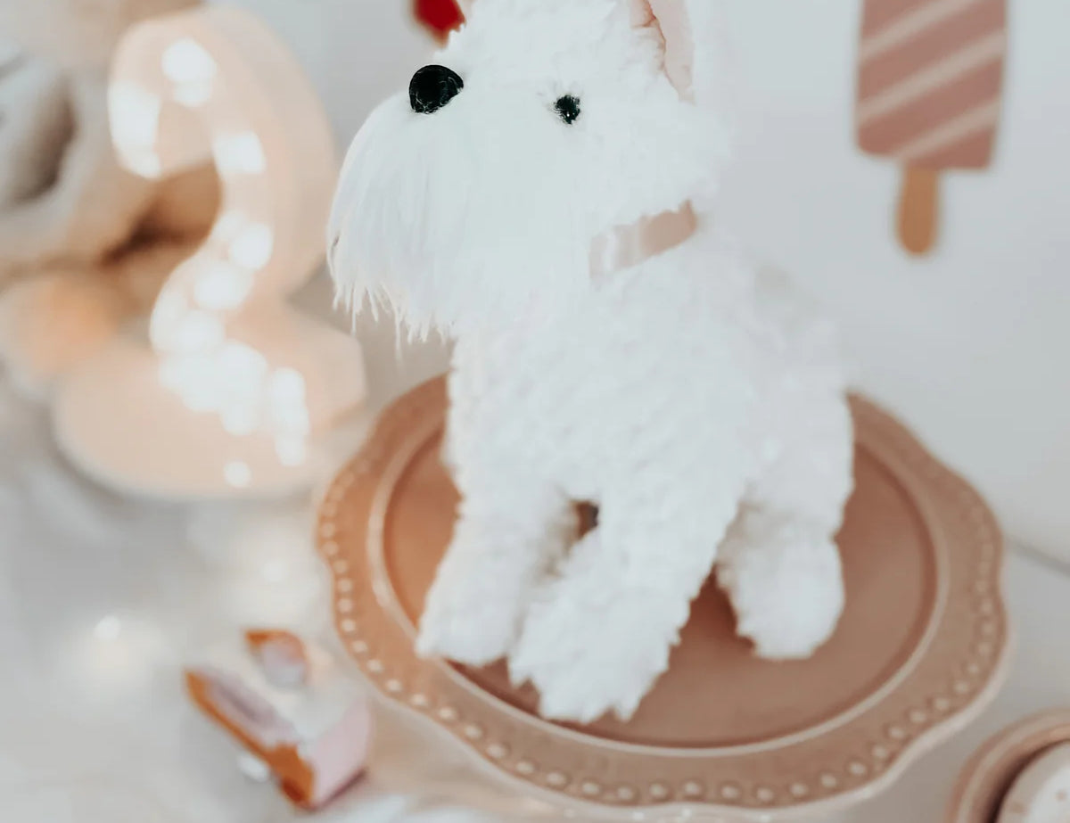 Mon Ami Wes The Westie plush sitting on a pink cake stand at a party
