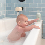 Mushie Bath Essentials Kit, a baby splashing in a white bathtub with blue tile