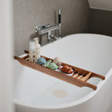 Mushie Bath Essentials Kit, pastel bath toys and bottles on a wooden bath tray over a white tub