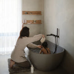 Mushie Bath Essentials Kit, a parent bathing a child in a grey freestanding tub