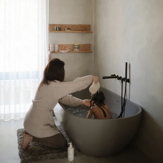Mushie Bath Essentials Kit, a parent bathing a child in a grey freestanding tub