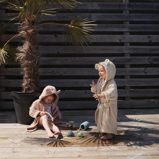 Mushie Bath Essentials Kit, two toddlers in robes playing with bath toys on a wooden deck