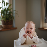 Laughing baby in a high chair chewing on a Mushie Blossom Suction Spinner Toy