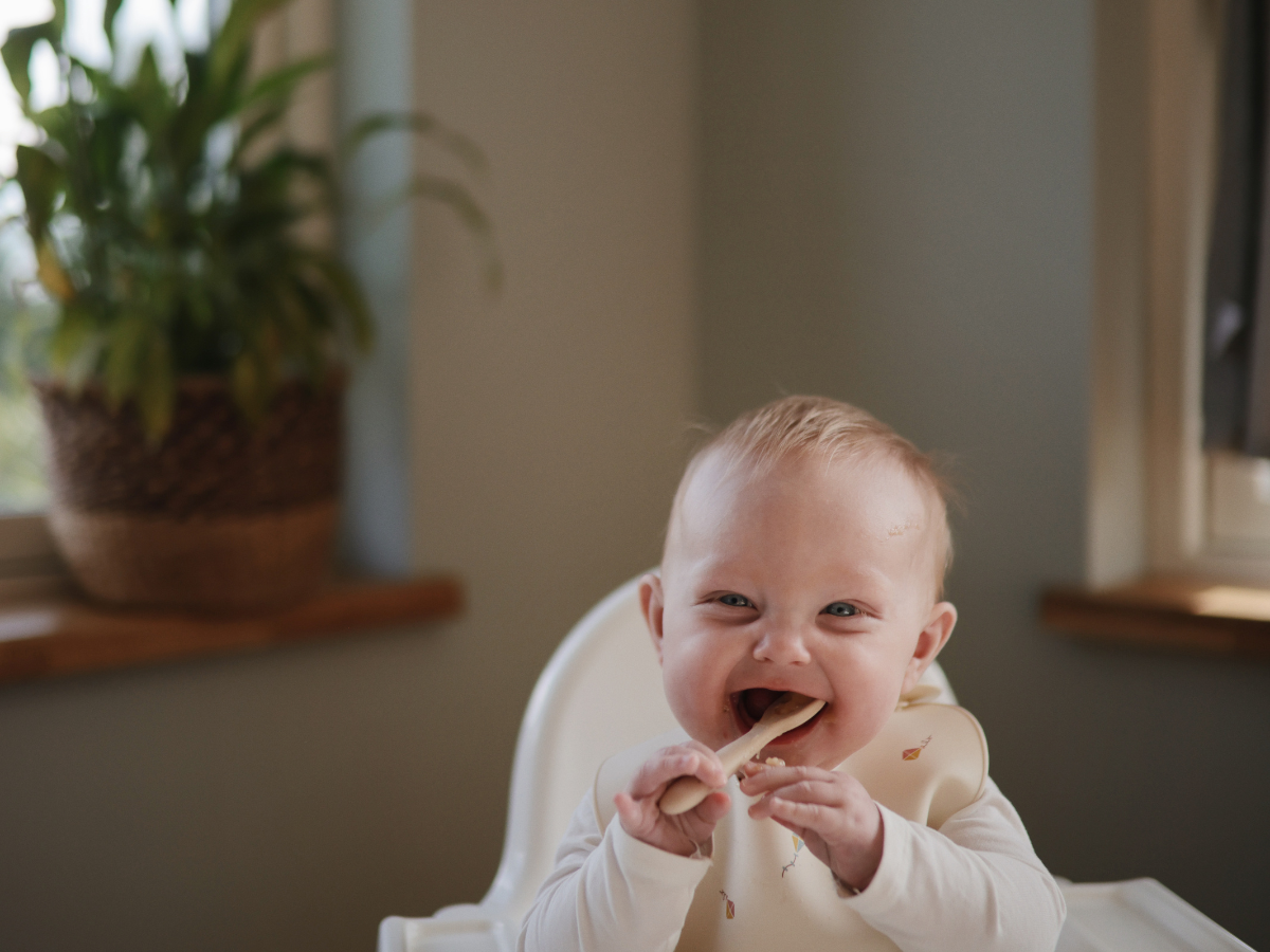 Laughing baby in a high chair chewing on a Mushie Blossom Suction Spinner Toy