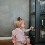 Toddler in pink spinning a Mushie Blossom Suction Spinner Toy stuck to a glass cabinet door