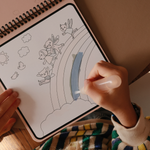 Child painting a rainbow on the Mushie Fairies Reusable Water Color Pad with the water brush