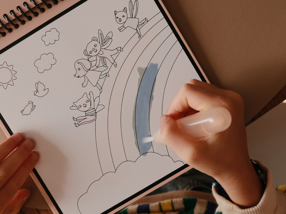 Child painting a rainbow on the Mushie Fairies Reusable Water Color Pad with the water brush