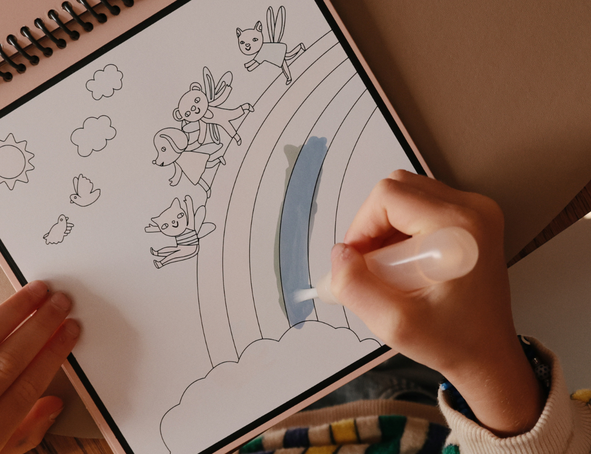 Child painting a rainbow on the Mushie Fairies Reusable Water Color Pad with the water brush