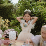 Girl in a tulle dress and flower crown at a garden table with the Mushie Fairies Reusable Water Color Pad
