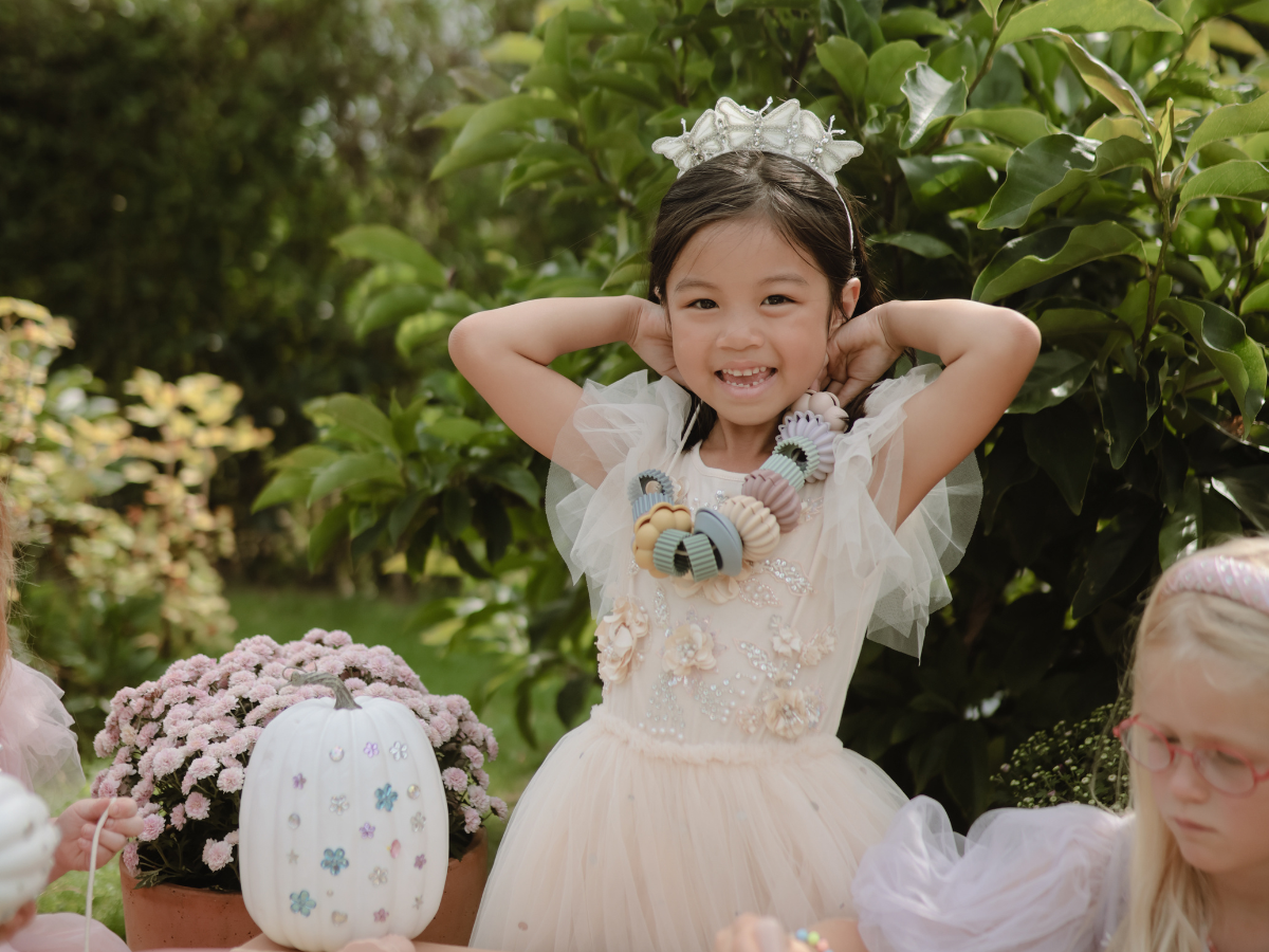 Girl in a tulle dress and flower crown at a garden table with the Mushie Fairies Reusable Water Color Pad