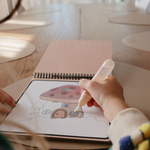 Close-up of a child's hand painting a mushroom fairy house on the Mushie Fairies Reusable Water Color Pad
