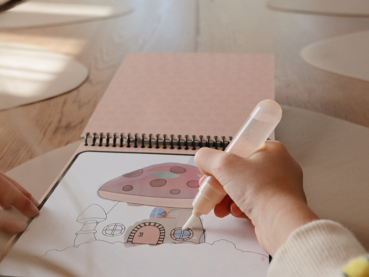 Close-up of a child's hand painting a mushroom fairy house on the Mushie Fairies Reusable Water Color Pad