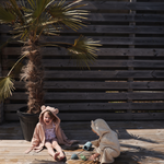 Two children in towels playing with the Mushie Mold Free Bath Play Set on a wooden deck