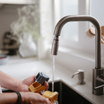 Hands rinsing a Mushie Mold Free Bath Play Set toy under a kitchen faucet