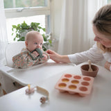 Baby in a high chair with the Mushie No-Drop Cactus Teether while a parent offers a snack