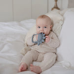 Baby lying on a bed chewing the Mushie No-Drop Dino Teether