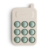 Mushie Phone Press Toy, a cream silicone toy phone with nine sage green pop-in number buttons
