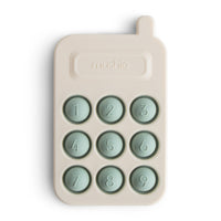 Mushie Phone Press Toy, a cream silicone toy phone with nine sage green pop-in number buttons
