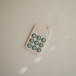 Mushie Phone Press Toy lying on a cream surface in soft light