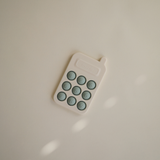 Mushie Phone Press Toy lying on a cream surface in soft light