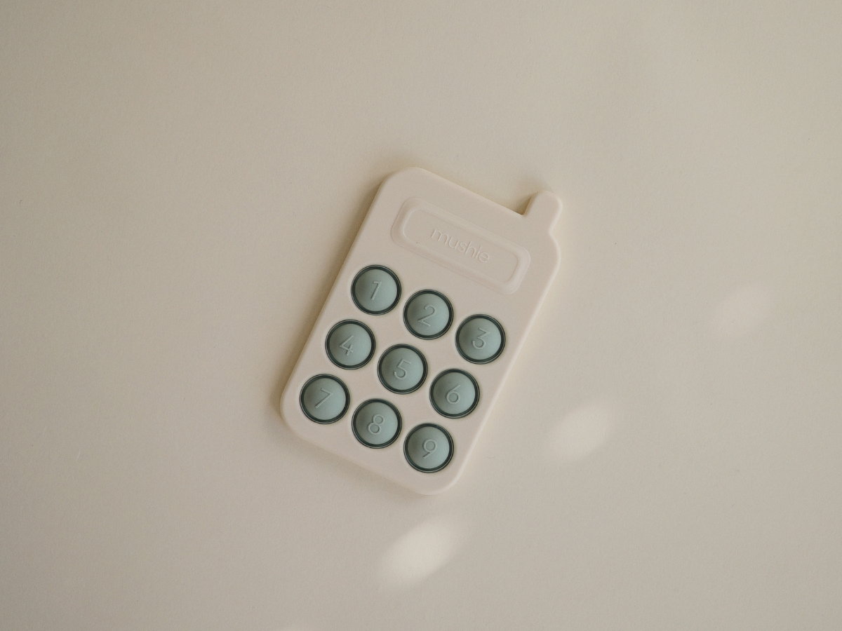 Mushie Phone Press Toy lying on a cream surface in soft light