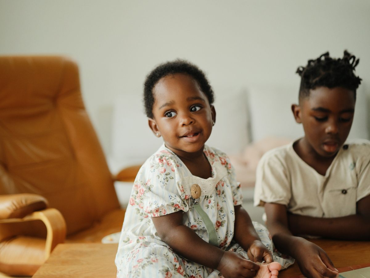 Two children sitting on a rug playing with Mushie toys in a living room