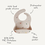 Mushie Silicone Baby Bib with feature callouts: food grade silicone, dishwasher safe, BPA free, deep pocket