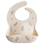 Mushie Silicone Baby Bib in Pink Flowers, a cream bib with a pink floral print and a catch pocket