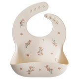 Mushie Silicone Baby Bib in Pink Flowers, a cream bib with a pink floral print and a catch pocket