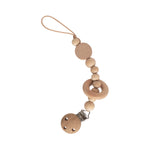 Mushie Silicone Pacifier Clip in Mila, natural wood beads and a ring on a tan strap with a wooden clip