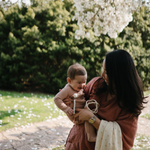 Mother holding a baby under a blossoming tree with a Mushie Silicone Pacifier Clip
