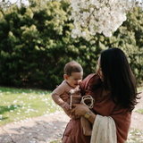 Mother holding a baby under a blossoming tree with a Mushie Silicone Pacifier Clip