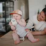 Baby in a cap drinking from the Mushie Silicone Training Cup in Whale while a parent smiles