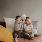 Toddler lifting a Mushie Snack Cup in Bluey Ivory overhead while sitting on a bed