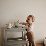 Toddler reaching for a Mushie Snack Cup in Bluey Sage on a step stool