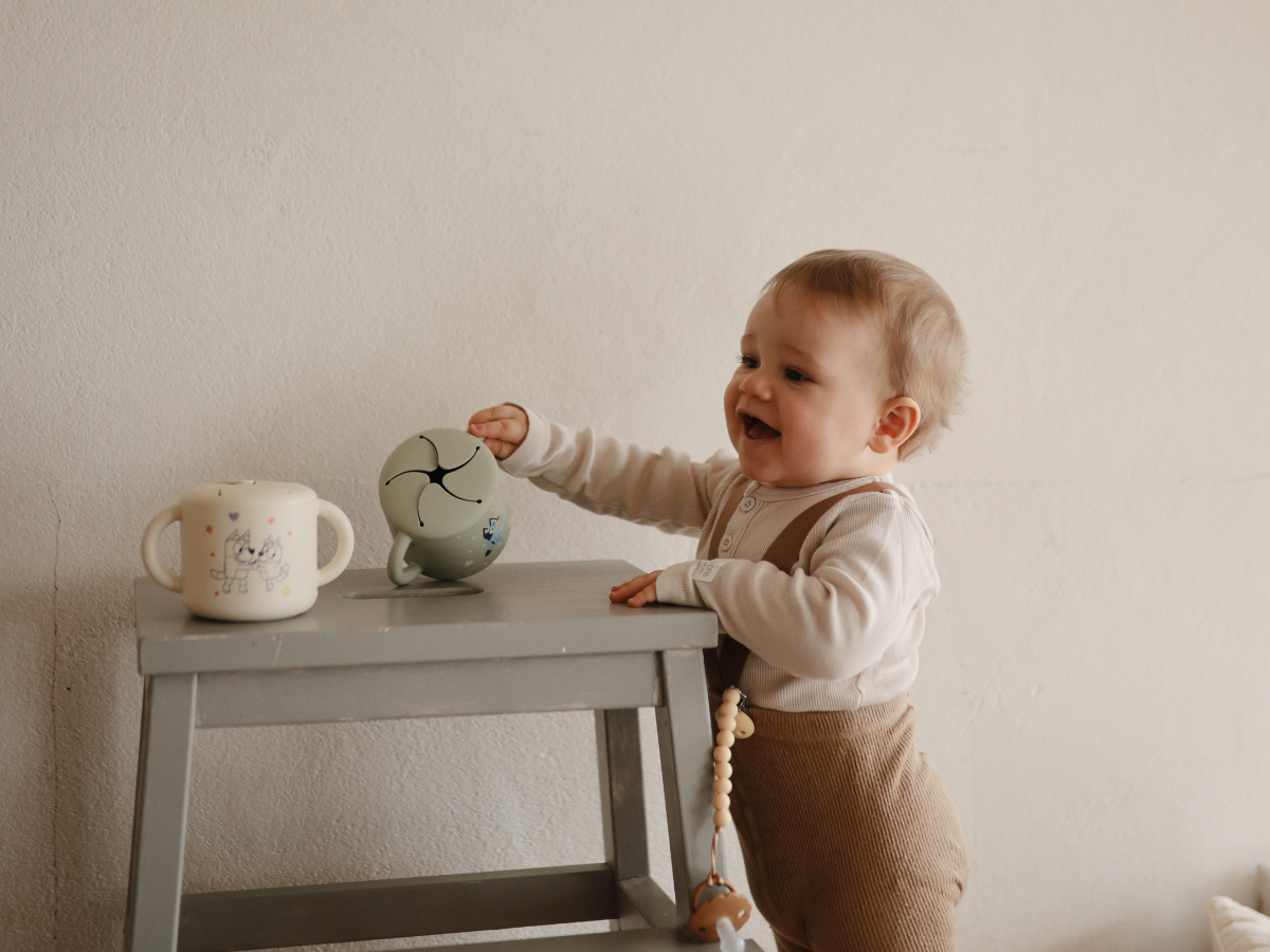 Toddler reaching for a Mushie Snack Cup in Bluey Sage on a step stool