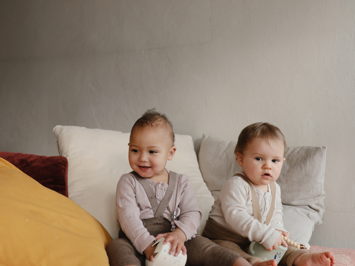 Two toddlers sitting on a bed with Mushie Snack Cups in Bluey prints
