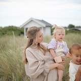 Mother holding a toddler with a Mushie Snack Cup in Blush in a grassy field