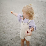 Toddler on a beach holding a Mushie Snack Cup in Blush