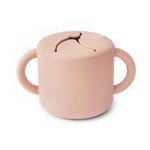 Mushie Snack Cup in Blush, a pink silicone cup with two handles and a slotted spill-proof lid